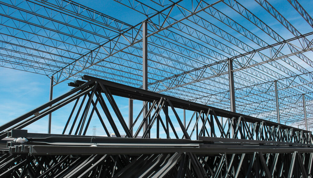 Looking up at steel joists under a blue sky before the roof has been laid.